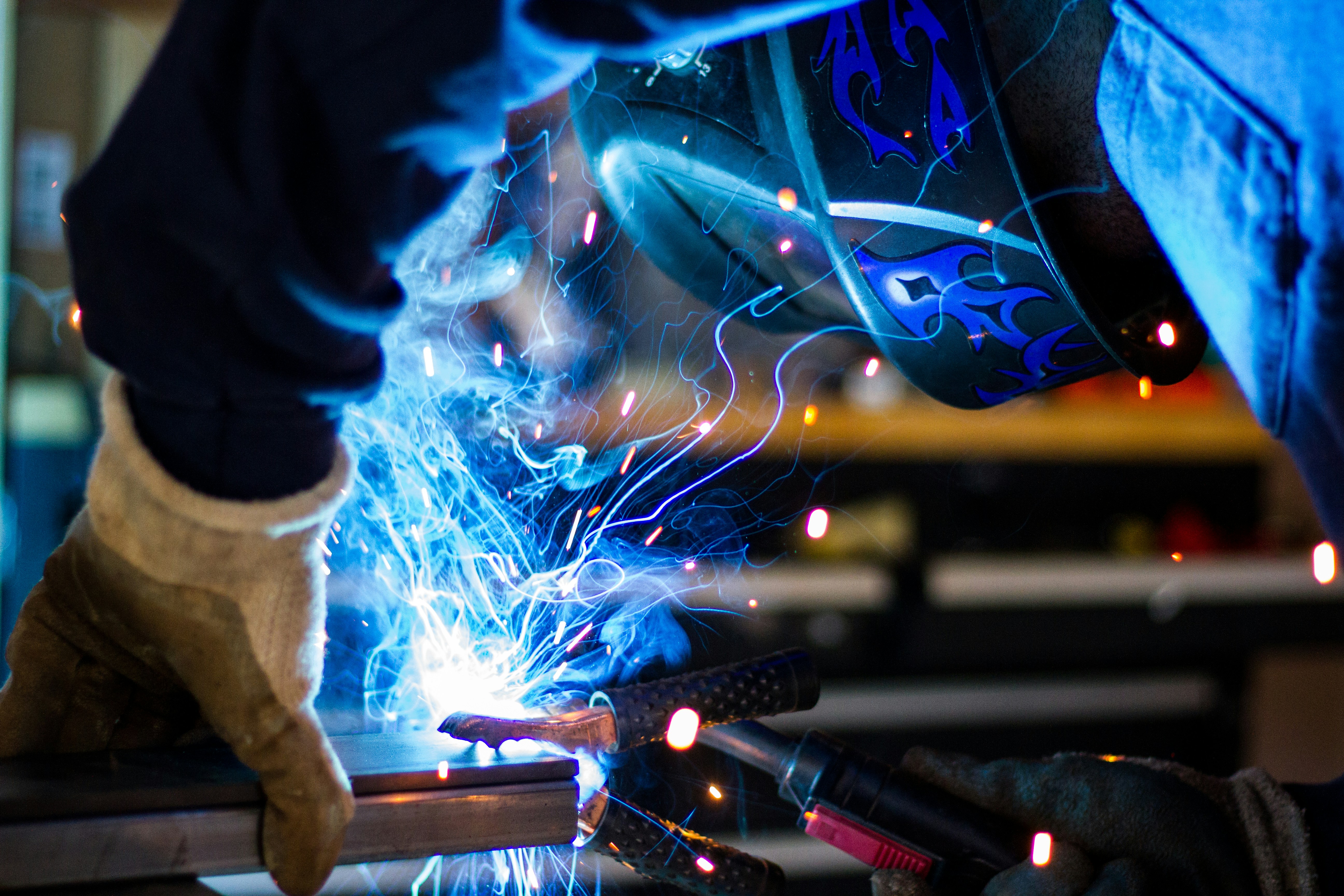 Welder in a flame-design helmet MIG welding steel as sparks fly